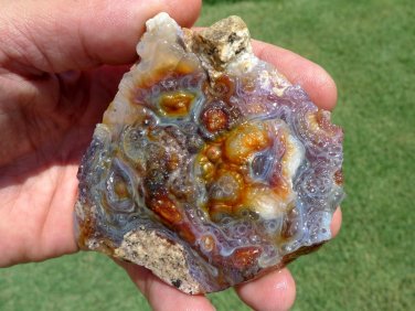Photo of an impressive piece of Arizona Fire Agate gemstone rough. It is an all natural specimen with wonderful fire banding across the face of the specimen, intricate chalcedony geometric designs, and a small area of druzy quartz crystals.